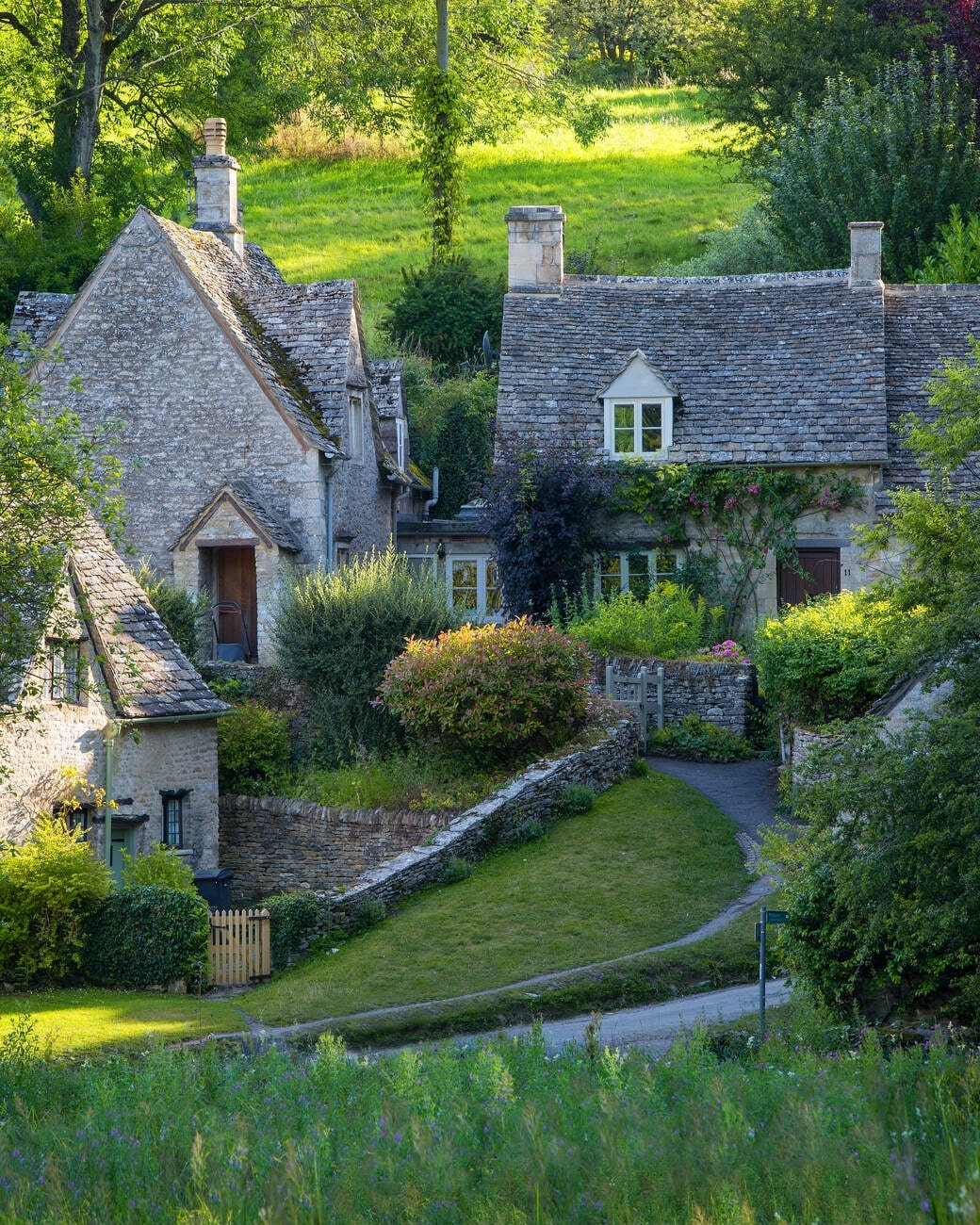 1. Bibury, Gloucestershire Bibury is often described as the most beautiful village in England, and it’s easy to see why. Located in the heart of the Cotswolds, Bibury is famous for its postcard-perfect row of 17th-century weavers' cottages known as Arlington Row. The cottages, with their honey-colored stone walls and steeply pitched roofs, make for one of the most photographed spots in the country. The River Coln runs through the village, adding to its charm, and you can enjoy a scenic walk or visit Bibury Trout Farm for some fresh local produce. Transportation Best accessed by car, though train services run to nearby Kemble Station, about 10 miles away. Local buses also connect to Bibury, but car rental is the most convenient option for exploring the surrounding countryside. Cuisine Bibury boasts traditional English pub fare. The Swan Hotel offers a delightful menu featuring locally sourced ingredients, with specialties such as Cotswold lamb and fresh trout from the nearby farm. Afternoon tea is also a popular treat here. Staying The Swan Hotel offers charming accommodations with riverside views, featuring cozy rooms, excellent service, and a classic English countryside atmosphere. There are also a few bed-and-breakfast options for a more intimate experience, Bibury, Gloucestershire